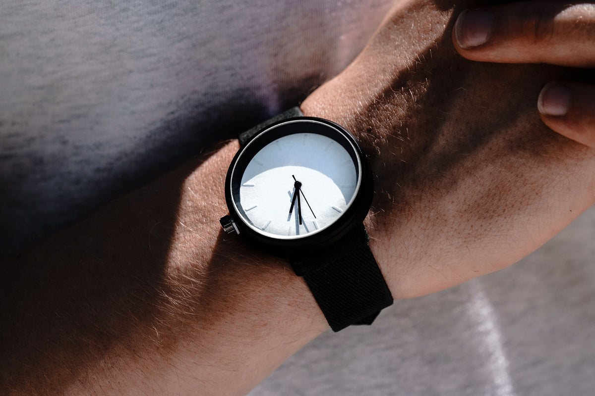 Man wearing a black strap watch; close-up of wrist with shadowed sunlit dial