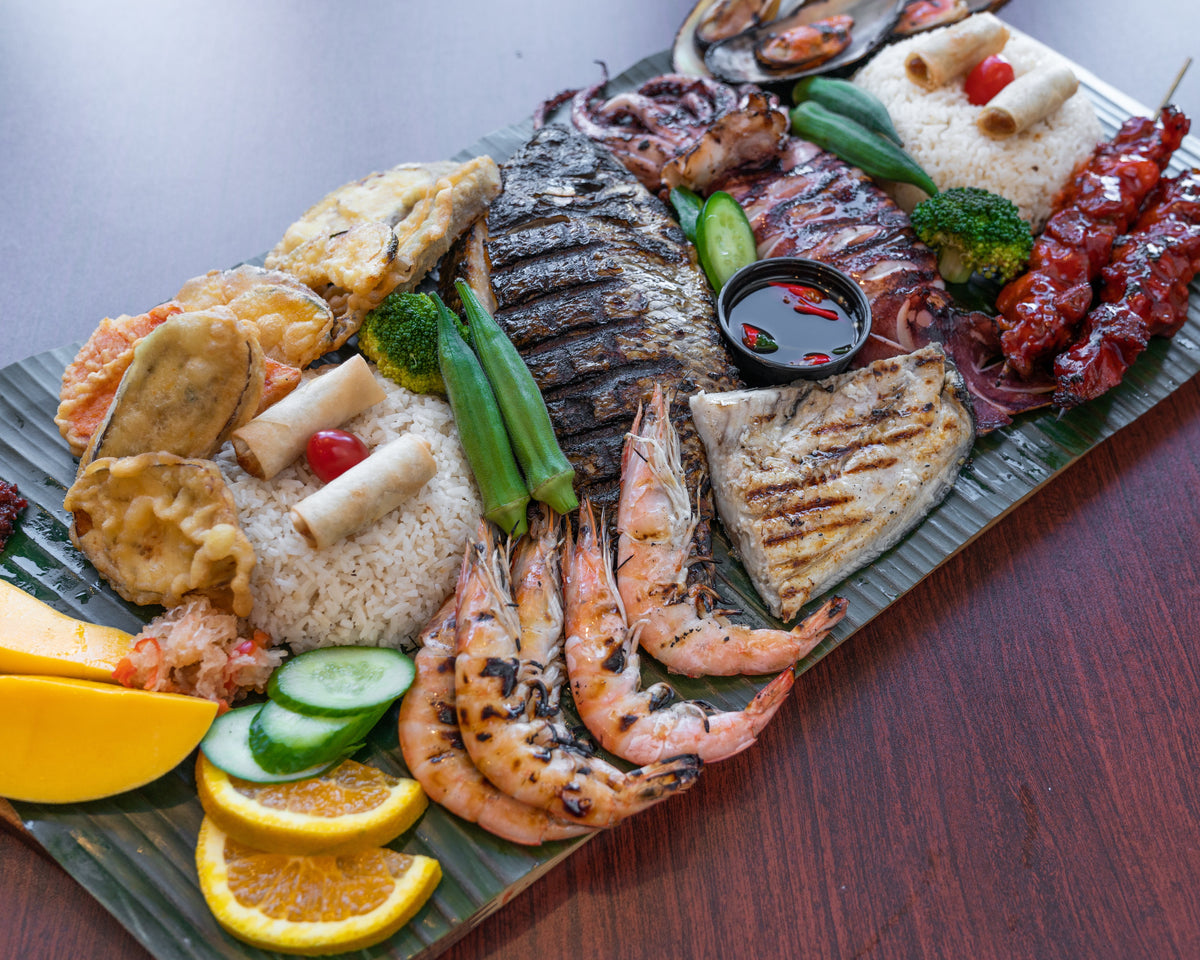 Seafood platter on banana leaf with rice, vegetables, citrus slices, shrimp, grilled fish, skewers, sauces